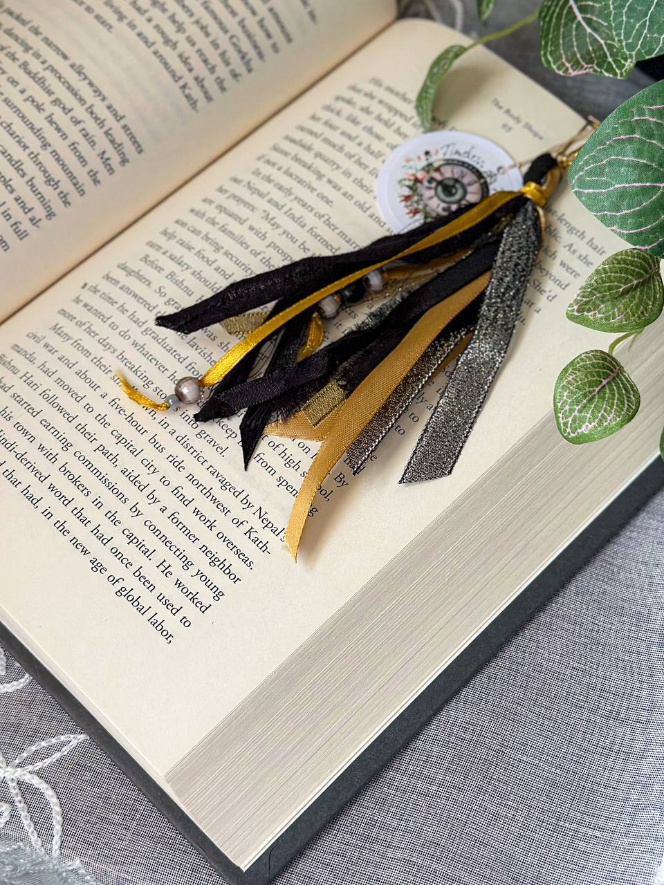 Handmade Boho tassel paperclip bookmark from Suzys Treasures, featuring black and gold lace ribbons, pearl bead accents, and crochet trim, displayed on an open book – a charming and versatile accessory for journals, planners, or novels.
