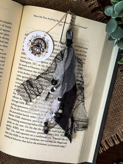 Handmade Boho tassel paperclip bookmark from Suzys Treasures, featuring black and white lace ribbons, pearl bead accents, and crochet trim, displayed on an open book – a charming and versatile accessory for journals, planners, or novels.