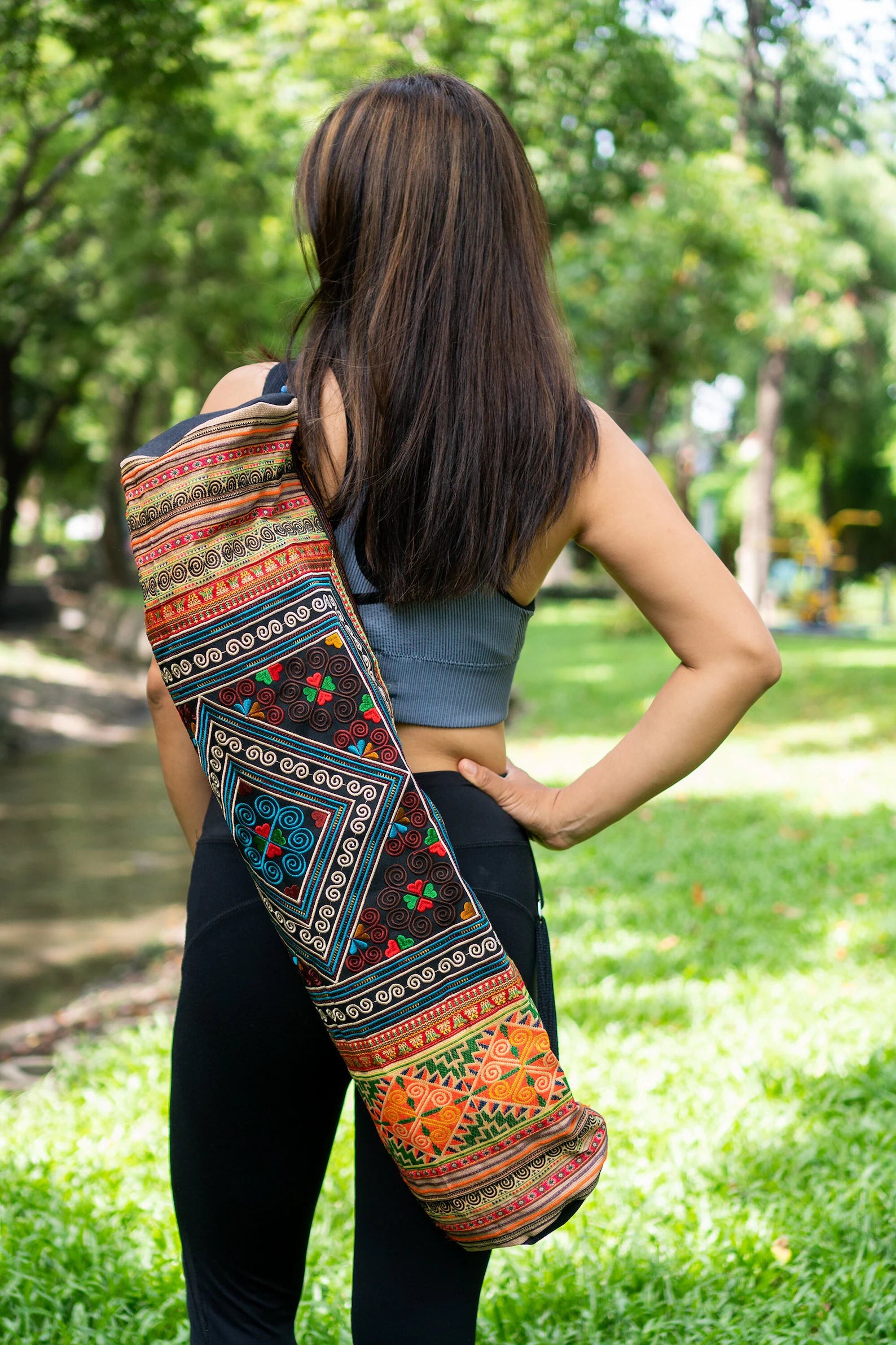 Woman carrying a colorful boho yoga bag with traditional ethnic patterns over her shoulder, standing outdoors surrounded by lush greenery – Suzys Treasures.